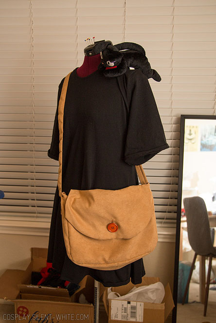 Black dress on a dressform with a brown suede bag over the shoulder